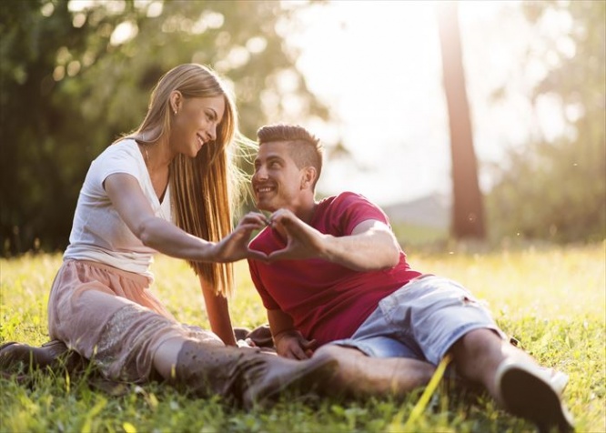 Young happy couple relaxing outdoors while making heart shape with their hands and looking at each other.