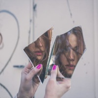 Beautiful redhead girl with long hair and blue eyes looking at herself in a broken mirror