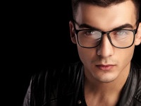 closeup portrait of shaved macho man in black leather jacket and white shirt wearing glasses while looking at the camera in isolated black studio background