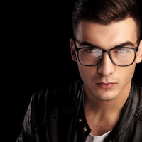 closeup portrait of shaved macho man in black leather jacket and white shirt wearing glasses while looking at the camera in isolated black studio background