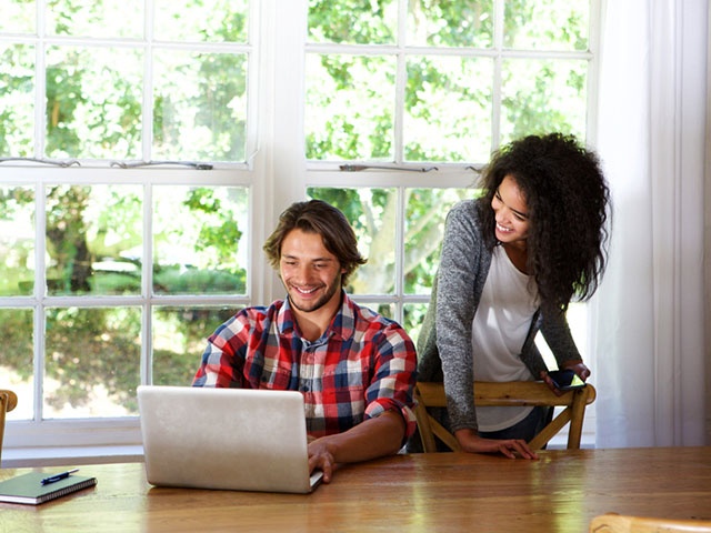Happy young couple sitting at table with laptop