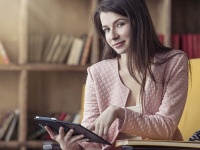 Beautiful young smart woman sits with the electronic book in the library on a chair