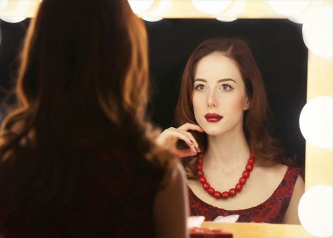 Portrait of a beautiful woman as applying makeup near a mirror.