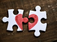 closeup of two separated pieces of a puzzle which together form a heart on a rustic wooden surface, depicting the idea of rupture or cooperation