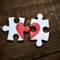 closeup of two separated pieces of a puzzle which together form a heart on a rustic wooden surface, depicting the idea of rupture or cooperation
