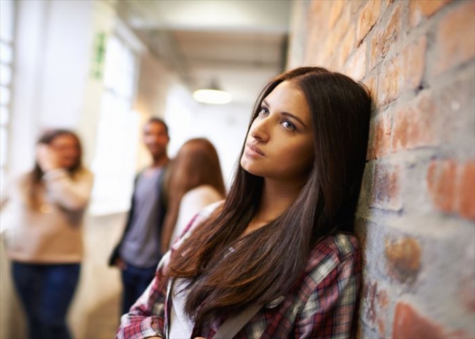 Shot of a bored-looking student standing in a hallway with her classmates in the background