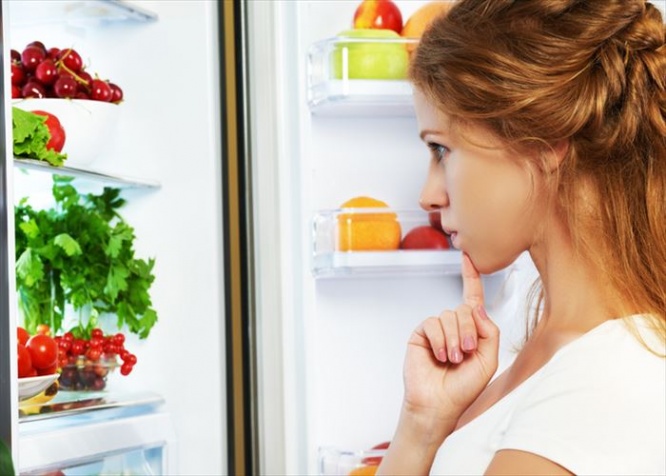 Happy woman standing at the open refrigerator with fruits, vegetables and healthy food
