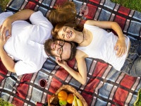 Top view of couple in love lying on a picnic blanket in the park with basket full of food and drinks placed next to them