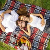 Top view of couple in love lying on a picnic blanket in the park with basket full of food and drinks placed next to them