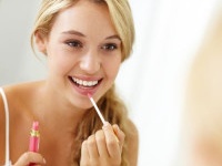 Lovely young woman applying lipgloss in front of a mirror