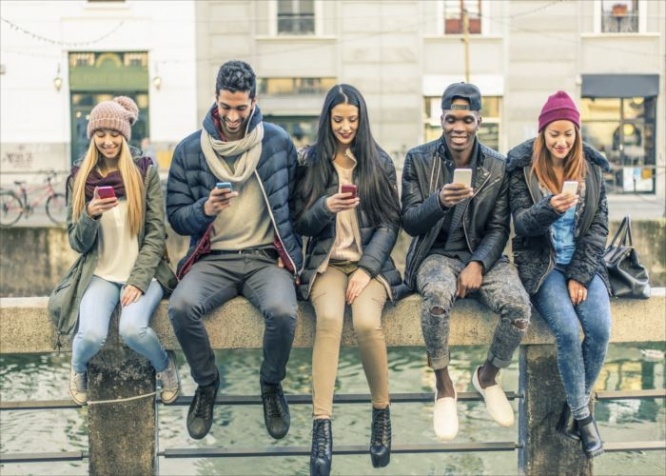 Multicultural group of friends using cellphones - Students sitting in a row and typing on the smartphones
