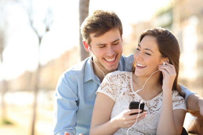 Couple listening to the music with earbuds from a smart phone in a park with an urban background