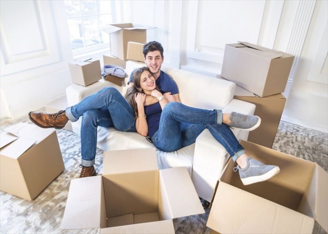 Moving, repairs, new flat. Couple in love hugging lying down and looking at the camera to move and wife hugging her husband while man and woman lying on the sofa among the boxes in an empty apartment