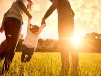 Happy family in the park evening light. The lights of a sun. Mom, dad and baby happy walk at sunset. The concept of a happy family.Parents hold the baby's hands.