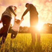 Happy family in the park evening light. The lights of a sun. Mom, dad and baby happy walk at sunset. The concept of a happy family.Parents hold the baby's hands.
