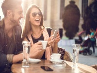 Young happy couple using cell phone while spending a day at a cafe.