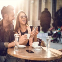 Young happy couple using cell phone while spending a day at a cafe.