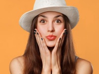 Surprised happy beautiful woman looking sideways in excitement. Excited girl in hat, isolated on orange background