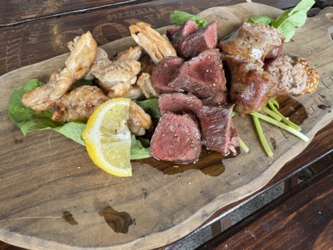 Sliced medium-rare steak and grilled chicken pieces on a wooden board with greens and a lemon wedge