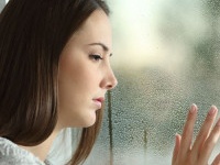 Sad woman looking rain through a window