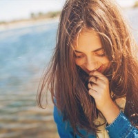 Shy girl sanding looking down. Cute teenage girl being shy on lake background. Film effect.