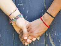 Two women holding hands with a wooden background. One is caucasian, the other is black. Multicultural, homosexual love and friendship concepts.