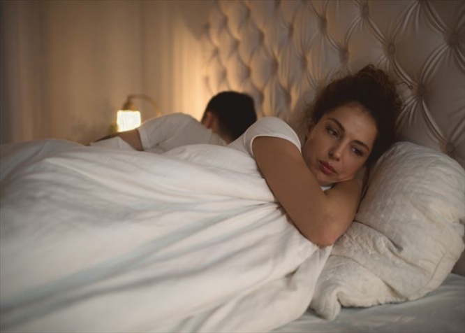 Worried young woman lying in bed away from her boyfriend.