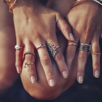 Cropped closeup of a boho girl's hands with many rings on her fingers, in gold and silver with dark blue stones
