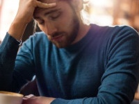 Young man with eyes closed having a headache while sitting in a cafe and holding his head in pain.