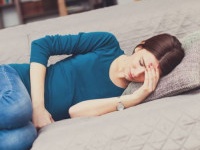 Young woman in pain, lying down on the couch in the living room