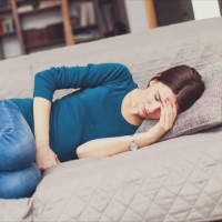Young woman in pain, lying down on the couch in the living room