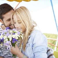 Loving couple riding Ferris wheel, woman holding flower bouquet
