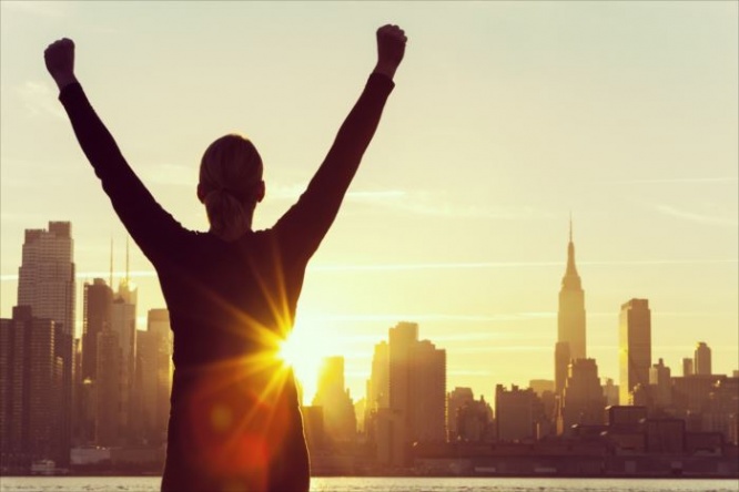 Instagram style filter silhouette of a successful woman or girl arms raised celebrating at sunrise or sunset in front of the New York City Skyline