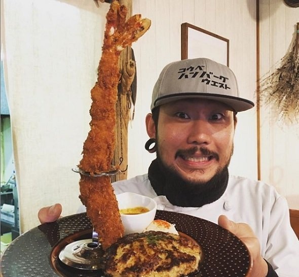 そびえ立つエビフライを持つ東店長（神戸ハンバーグウエストのInstagramより）