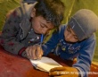 レバノンの非公式テント居住区で、友達に教えてもらいながら文字を書く練習をするシリア難民の子ども。© UNICEF_NYHQ2013-1389_Noorani