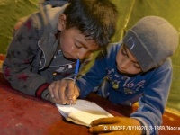 レバノンの非公式テント居住区で、友達に教えてもらいながら文字を書く練習をするシリア難民の子ども。© UNICEF_NYHQ2013-1389_Noorani