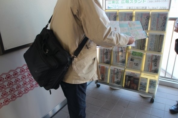 観光パンフレットを手に取るM記者。なお、英語パンフでは豊洲新市場は「11月オープン」と記されていた
