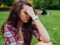 Girl sitting in  the park on the grass. She has headache. What a terrible day