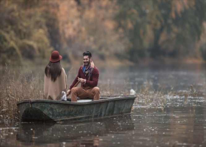 Young happy man paddling a boat during autumn day and talking to his girlfriend.