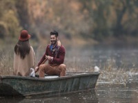 Young happy man paddling a boat during autumn day and talking to his girlfriend.