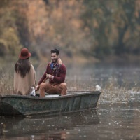 Young happy man paddling a boat during autumn day and talking to his girlfriend.