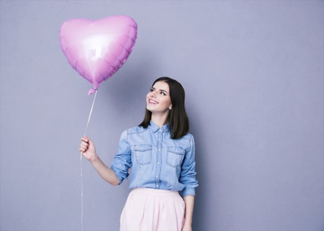 Happy woman holding balloon over gray background. Lookign away.