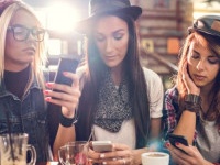 Female friends sitting in a cafe while each of them is using their own cell phone.