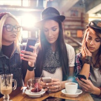 Female friends sitting in a cafe while each of them is using their own cell phone.