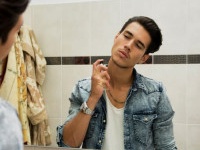 Handsome young man in his home bathroom, spraying cologne or perfume on neck