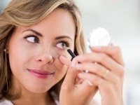 Beautiful portrait of a woman applying eyeliner and looking in a compact mirror - makeup concepts