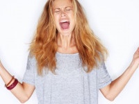 A pretty young girl yelling out in frustration with her fists raised - white background