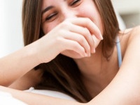 Laughing vivacious young woman with her hand to her mouth in a candid moment, close up head and shoulders