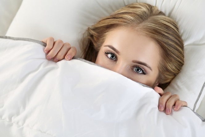 Beautiful blonde woman hiding face under cover lying in bed. Female sparky eyes looking in camera closeup. Sweet dreams, flirtation, playing game, wake up in strange place, shame, casual sex concept