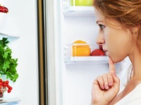 Happy woman standing at the open refrigerator with fruits, vegetables and healthy food